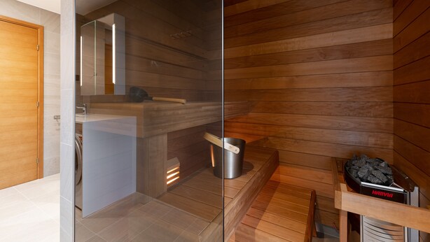 Um banheiro moderno com divisória de vidro, área de sauna em madeira e aquecedor de sauna.