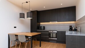 Uma cozinha moderna com armários escuros, uma mesa de jantar de madeira e duas luminárias pendentes.