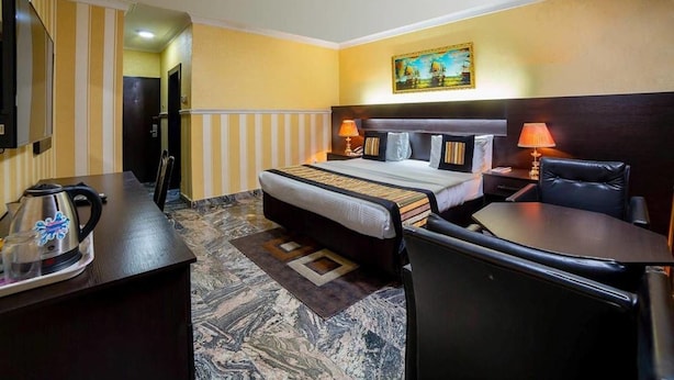 A hotel room with a bed, bedside table, lamp, chair, desk, and a television. - Landmark Hotel (Port Harcourt)