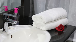 A bathroom with a white sink, a mirror, a black countertop, and a red rose. - Landmark Hotel (Port Harcourt)