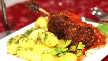 Un plat amb una cuixa de xai rostida, patates bullides i una salsa de tomàquet.