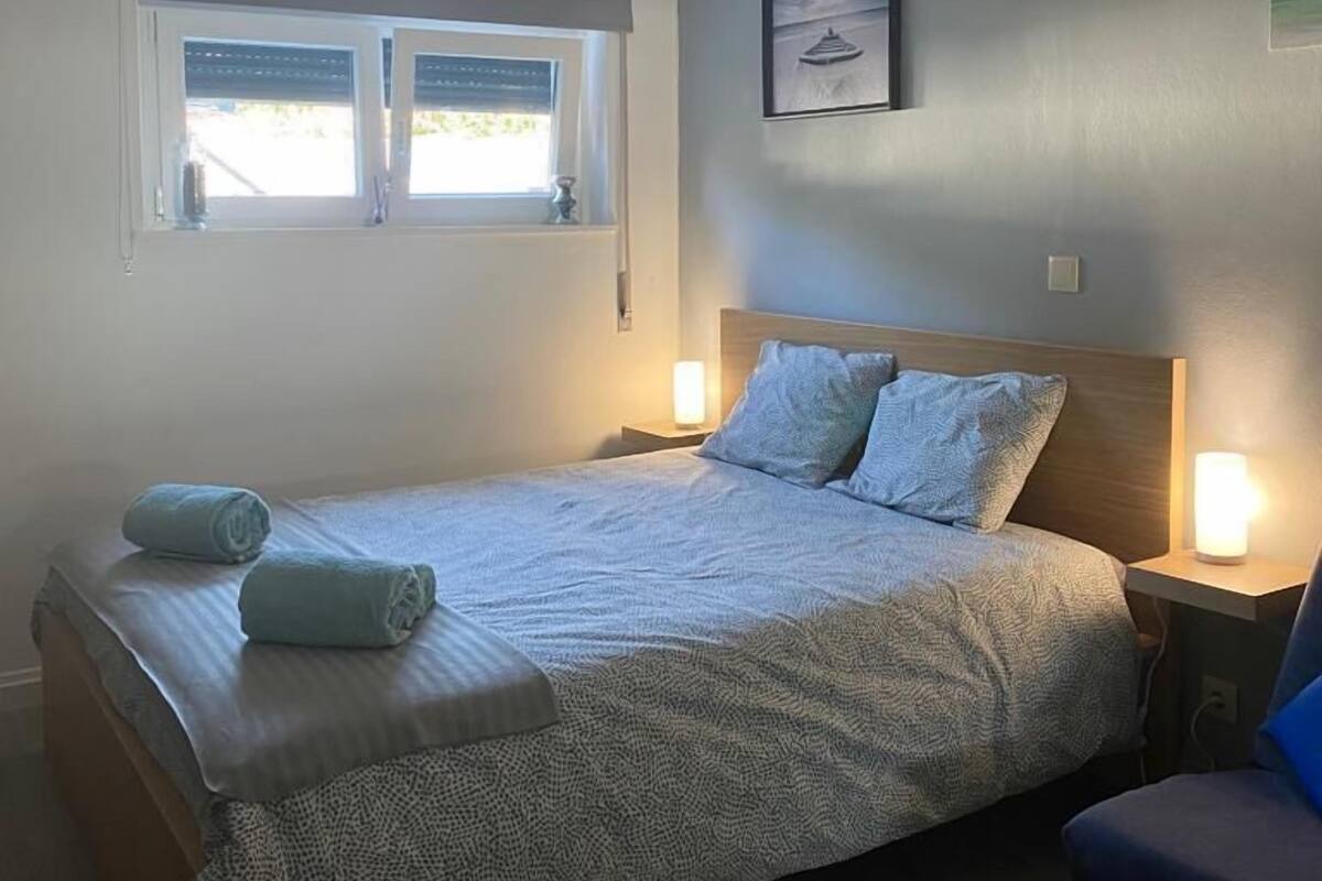 Un dormitorio con cama, dos lámparas de noche, una ventana con persianas y un cuadro colgado en la pared.
