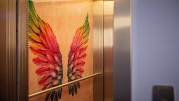 An elevator interior with a mural of colorful bird wings on the wall.