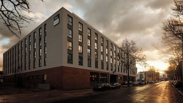A modern building with a brick facade and multiple windows, located on a street with parked cars and trees.