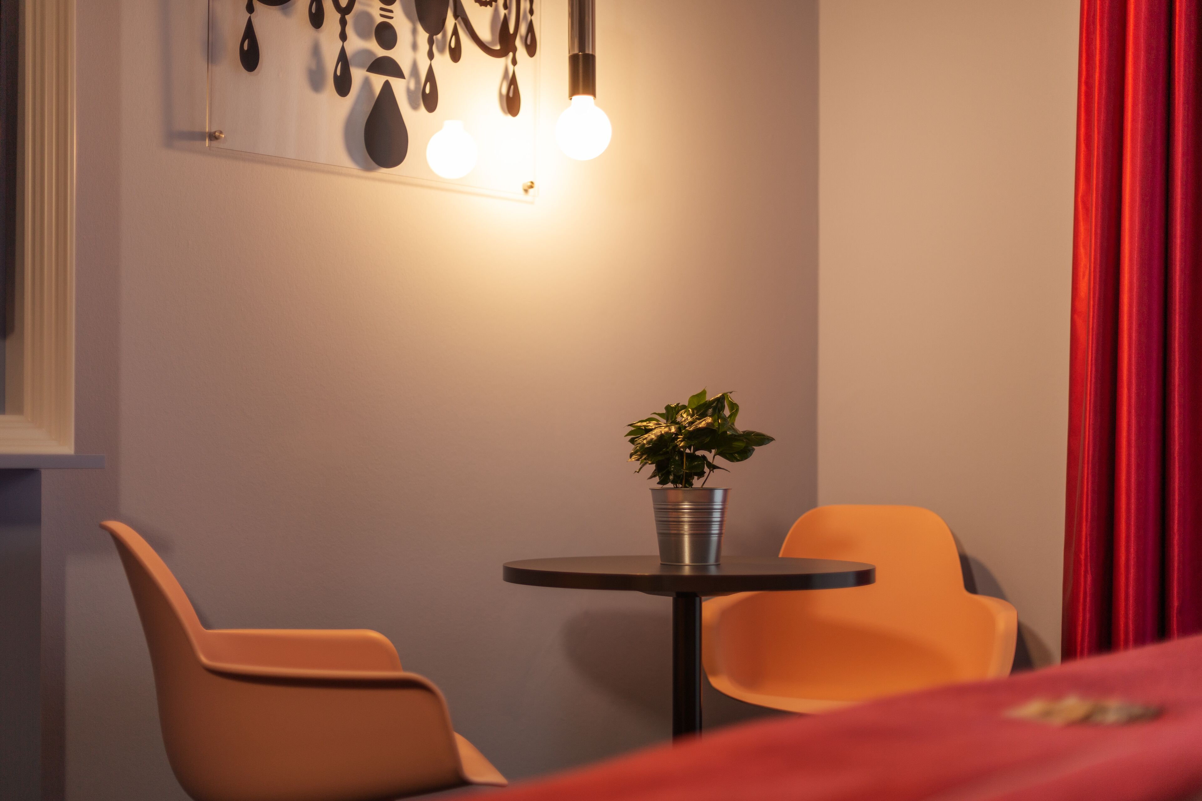 Une pièce avec une table ronde, deux chaises, une plante en pot et un luminaire fixé au mur.