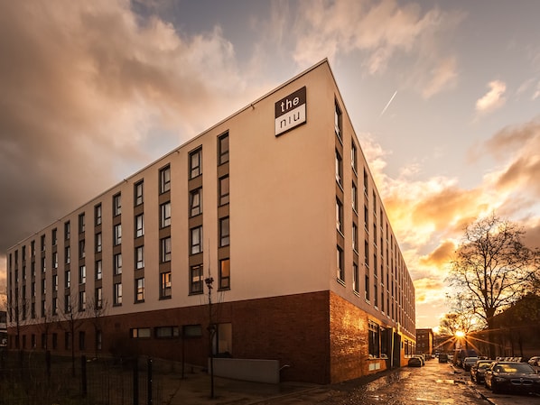A modern building with a sign reading "the niu" on the side. It features a row of windows and a brick base.