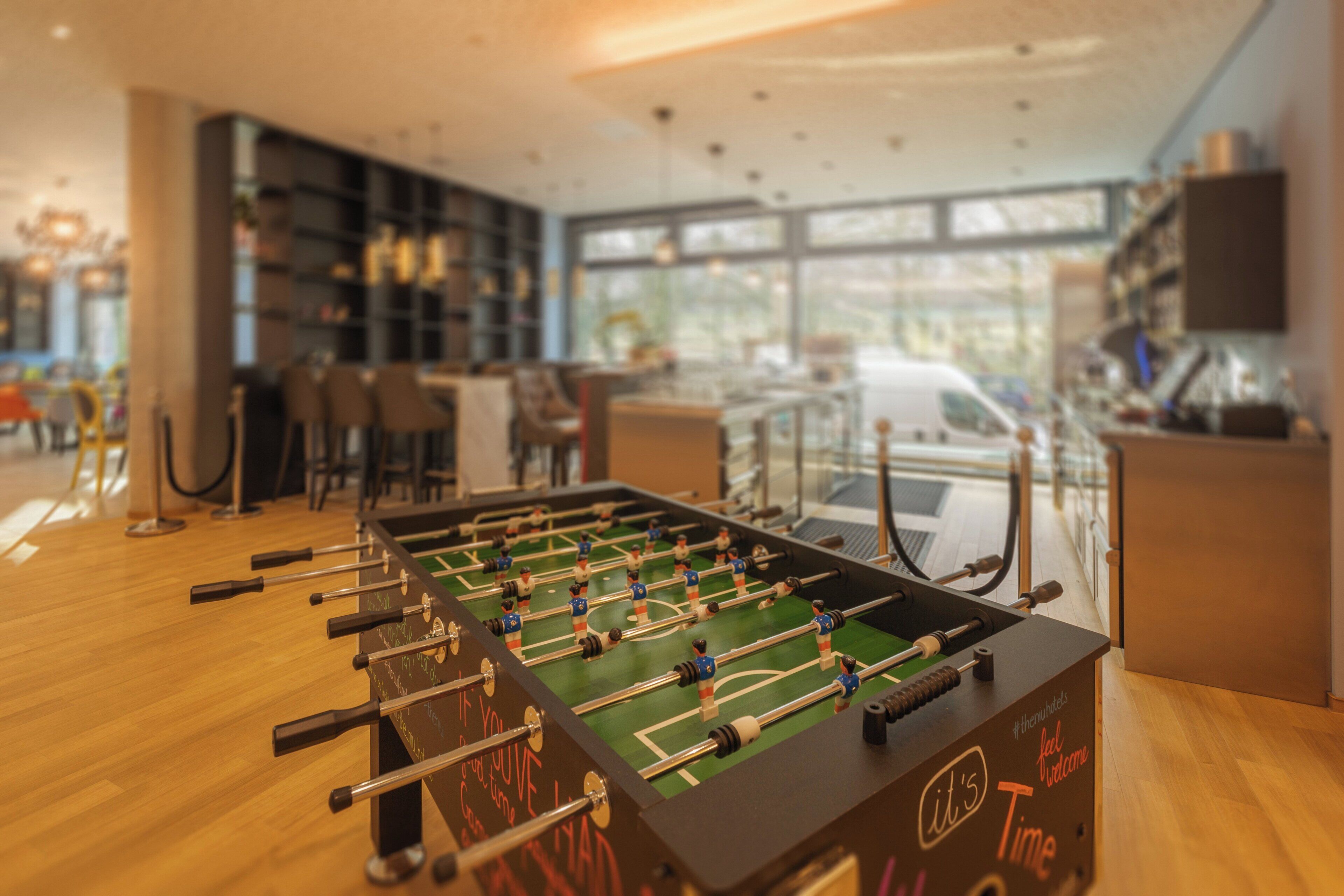 Una mesa de fútbolín en una habitación moderna con suelo de madera, una estantería y un ventanal grande.
