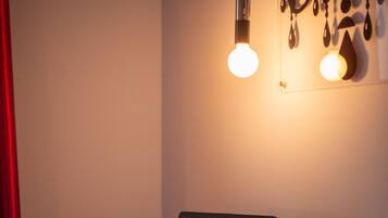 A laptop on a small round table with two orange chairs, a red curtain, and a wall with hanging light fixtures.