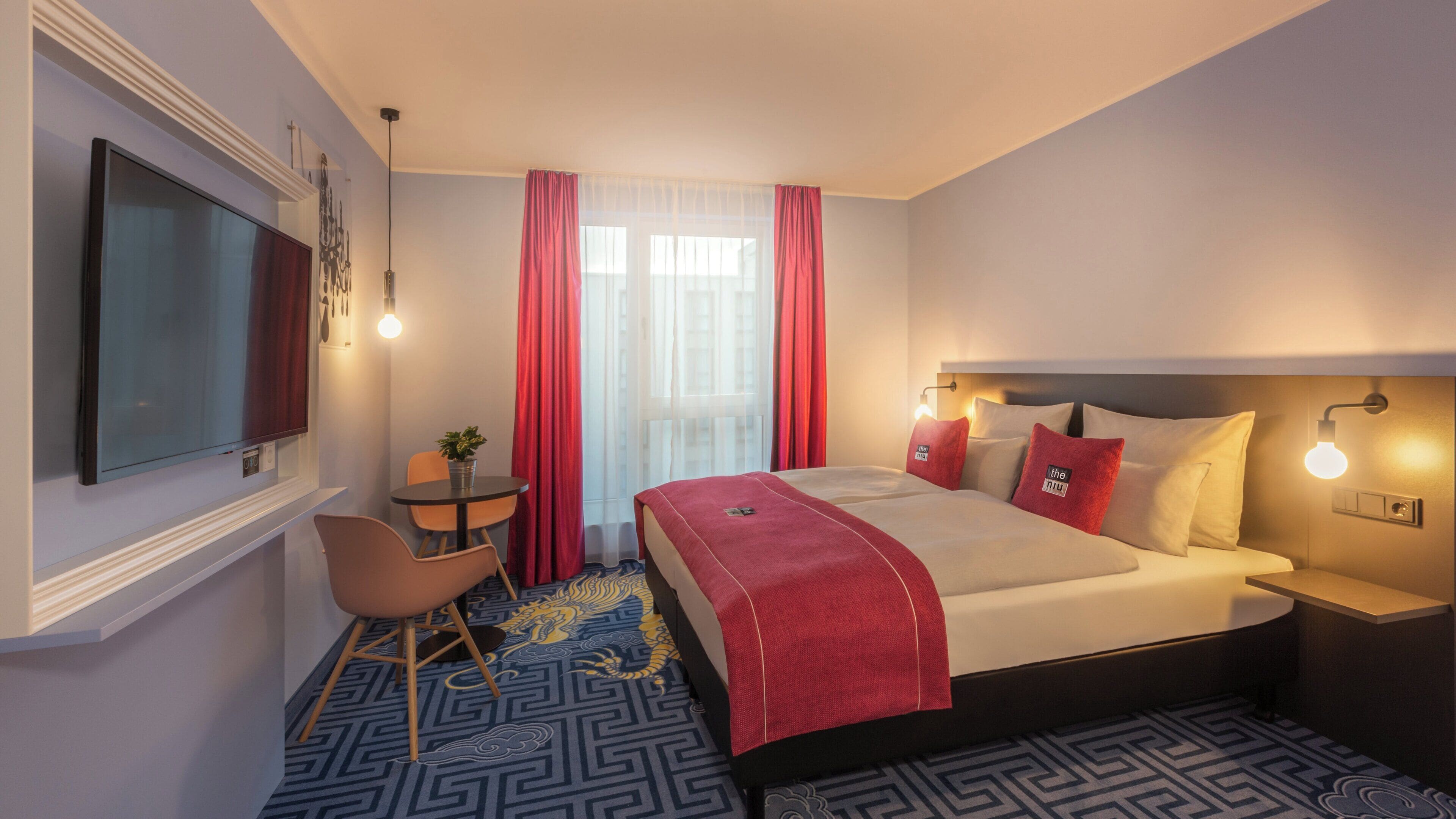 A hotel room with a bed, a desk, a chair, a TV, and a window with curtains.