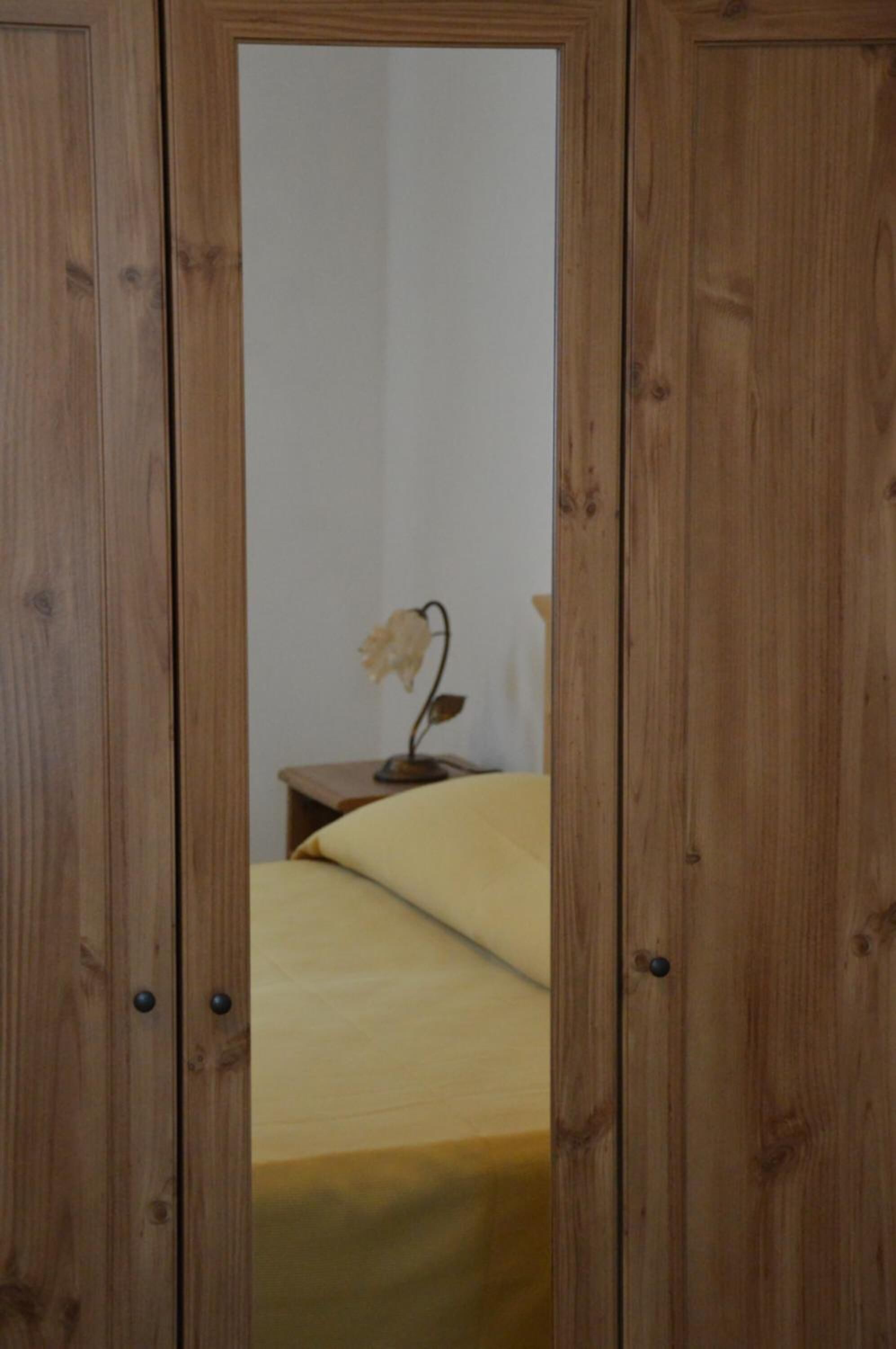 A wooden wardrobe with a mirror, a bed with a yellow bedspread, and a small table with a lamp.