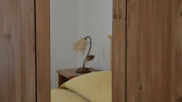 A wooden wardrobe with a mirror, a bed with a yellow bedspread, and a small table with a lamp.