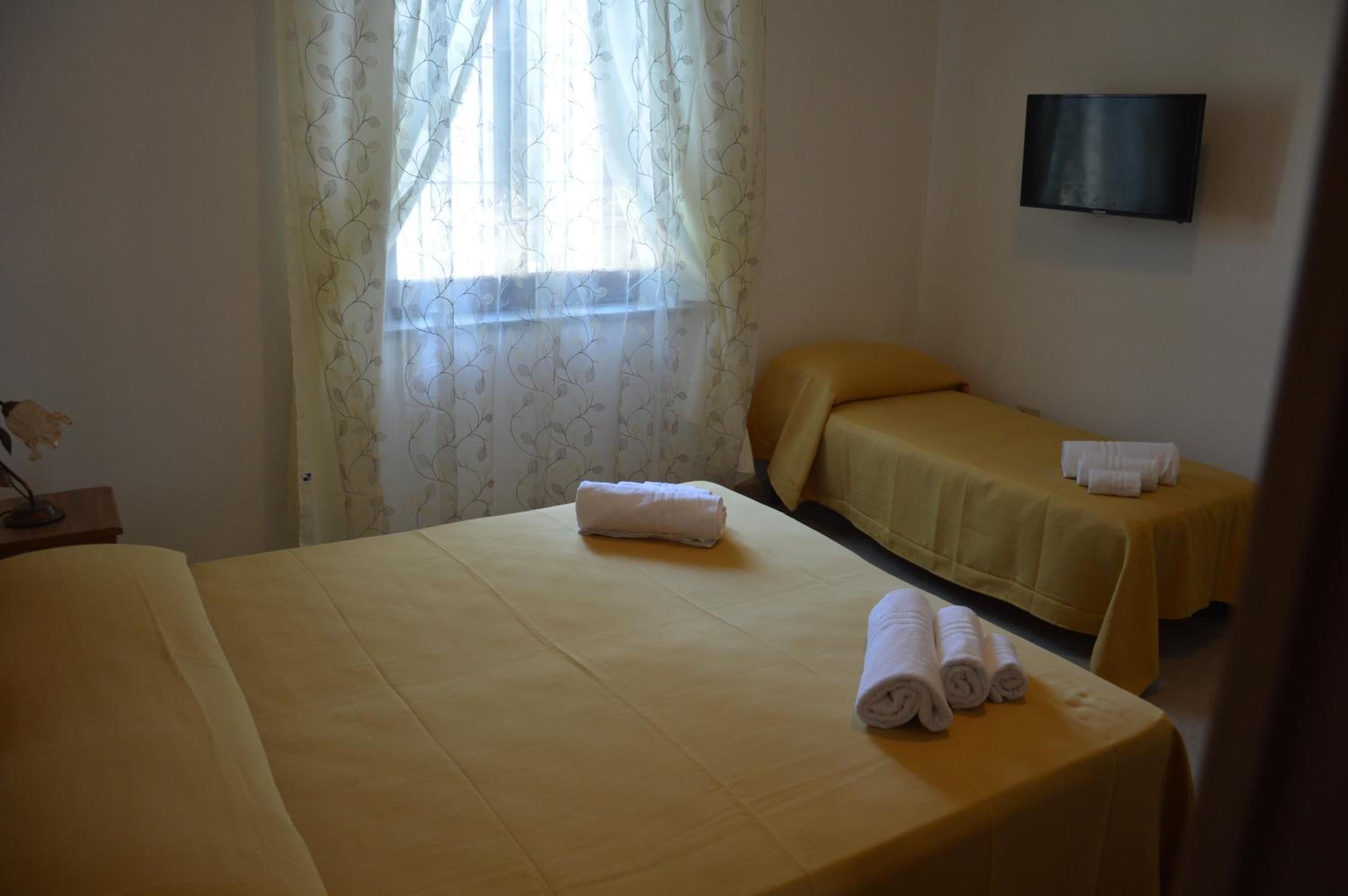 Une chambre d’hôtel avec deux lits, un téléviseur fixé au mur et une fenêtre avec des rideaux légers.