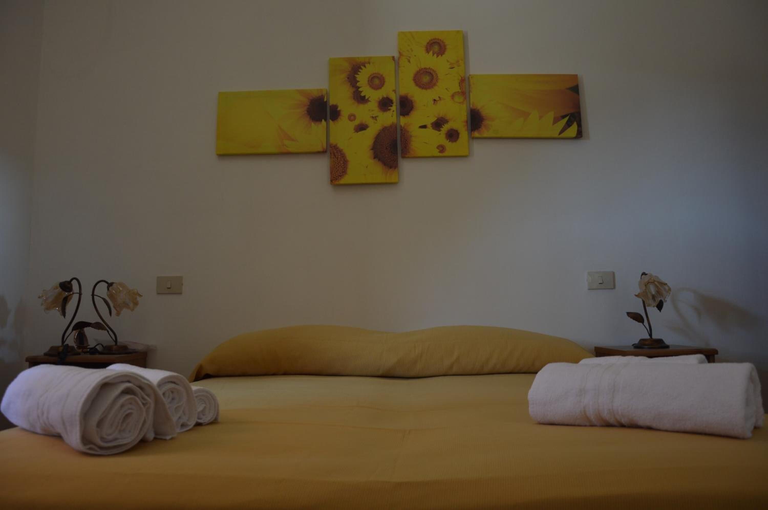 A hotel room with a bed, two nightstands, a wall-mounted painting, and rolled towels.