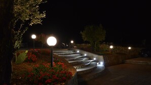 A nighttime outdoor area with a curved pathway, stone steps, and illuminated street lamps.