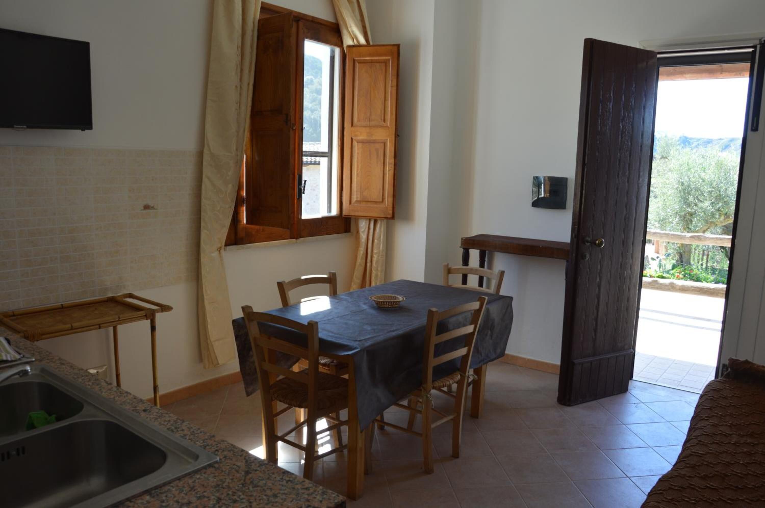 Zona pranzo con tavolo e sedie, una finestra con tende, angolo cottura con lavello e una porta che dà all'esterno.