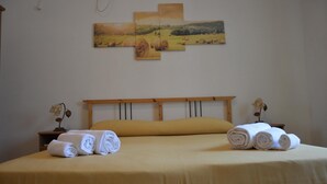 A neatly made bed with rolled towels, a wooden headboard, and a wall-mounted painting of a landscape.