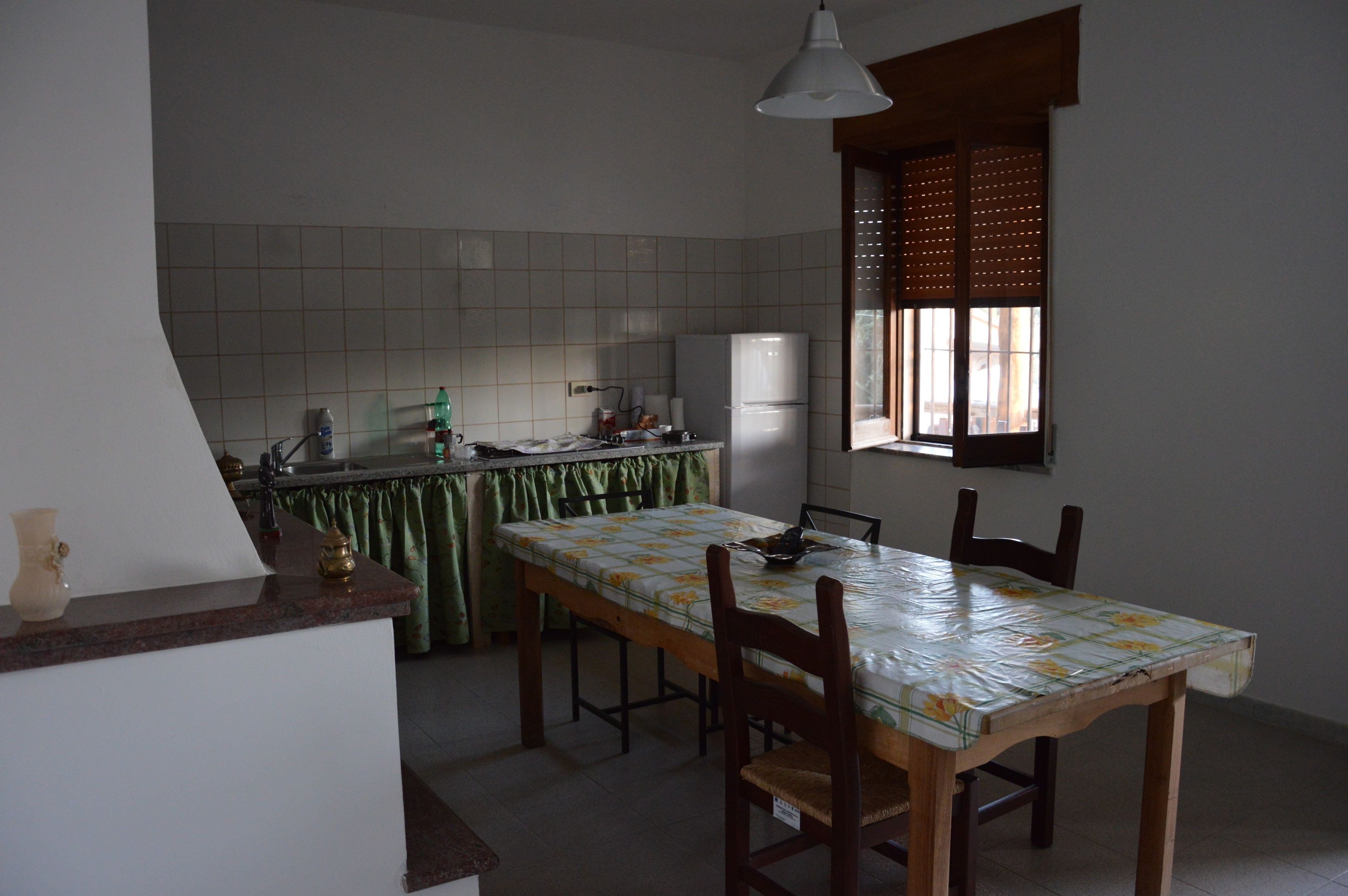 Eine Küche mit Esstisch, Stühlen, einem Kühlschrank und einem Fenster mit Jalousien.