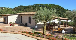 Un edificio de piedra con ventanas arqueadas, un patio empedrado con flores y una estructura de madera con techo.