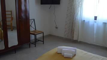 A room with a bed, a wooden wardrobe, a chair, a television mounted on the wall, and a window with curtains.