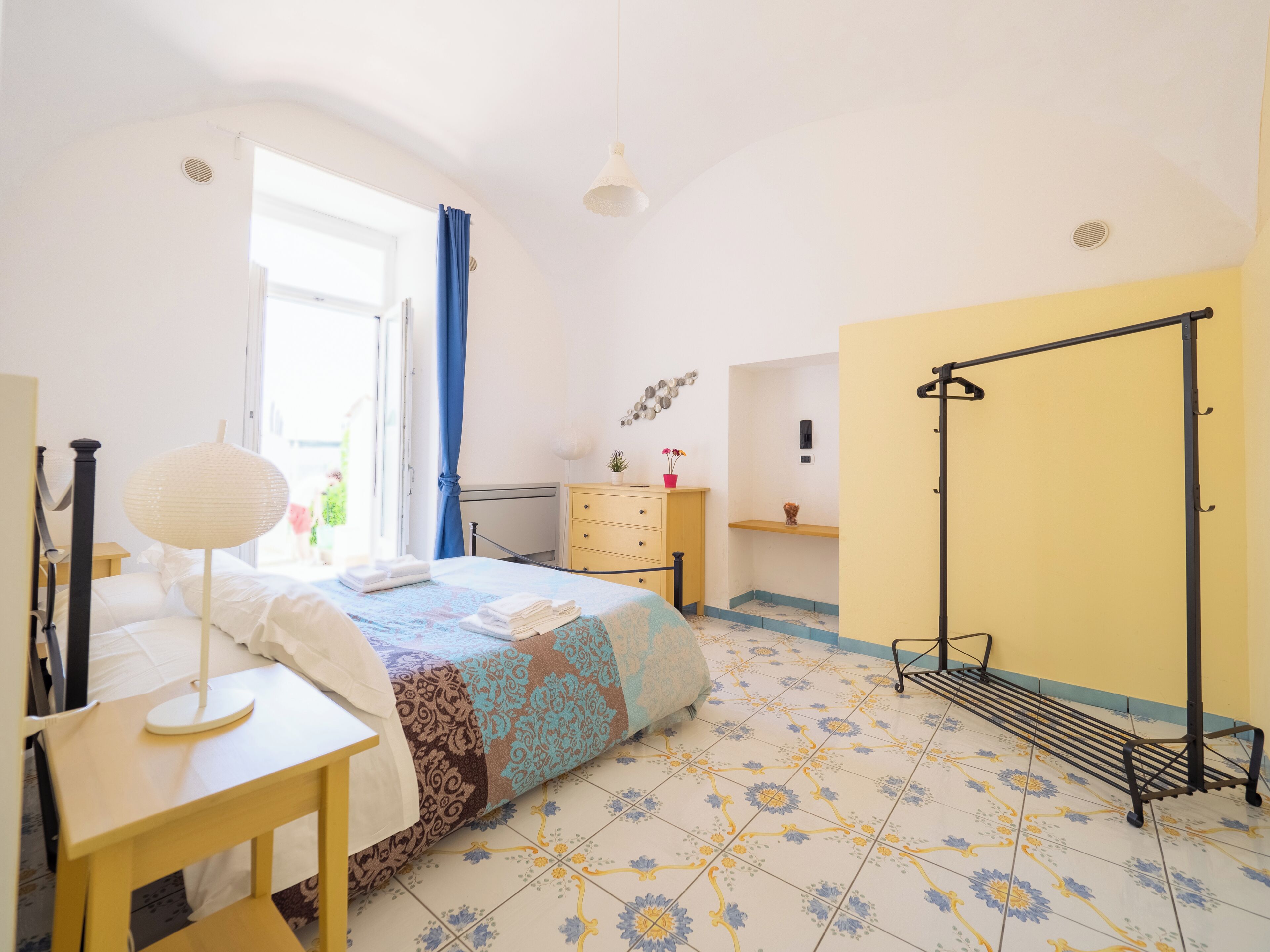 A bedroom with a bed, a desk, a wardrobe, and a hanging rack.
