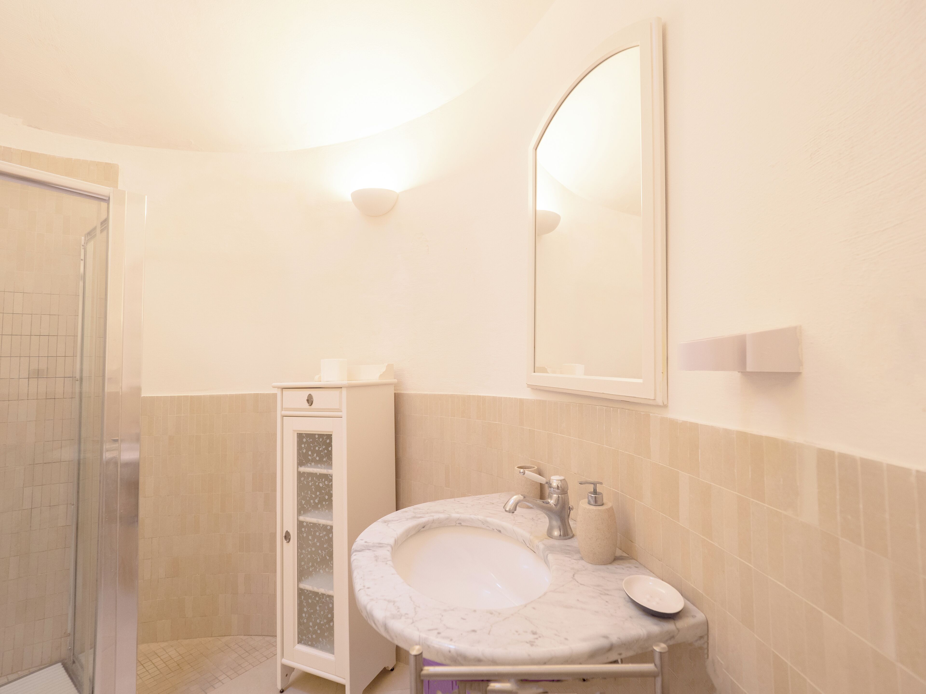 Une salle de bain dotée d’un lavabo en marbre, d’une cabine de douche en verre et d’un meuble avec une porte en verre dépoli.
