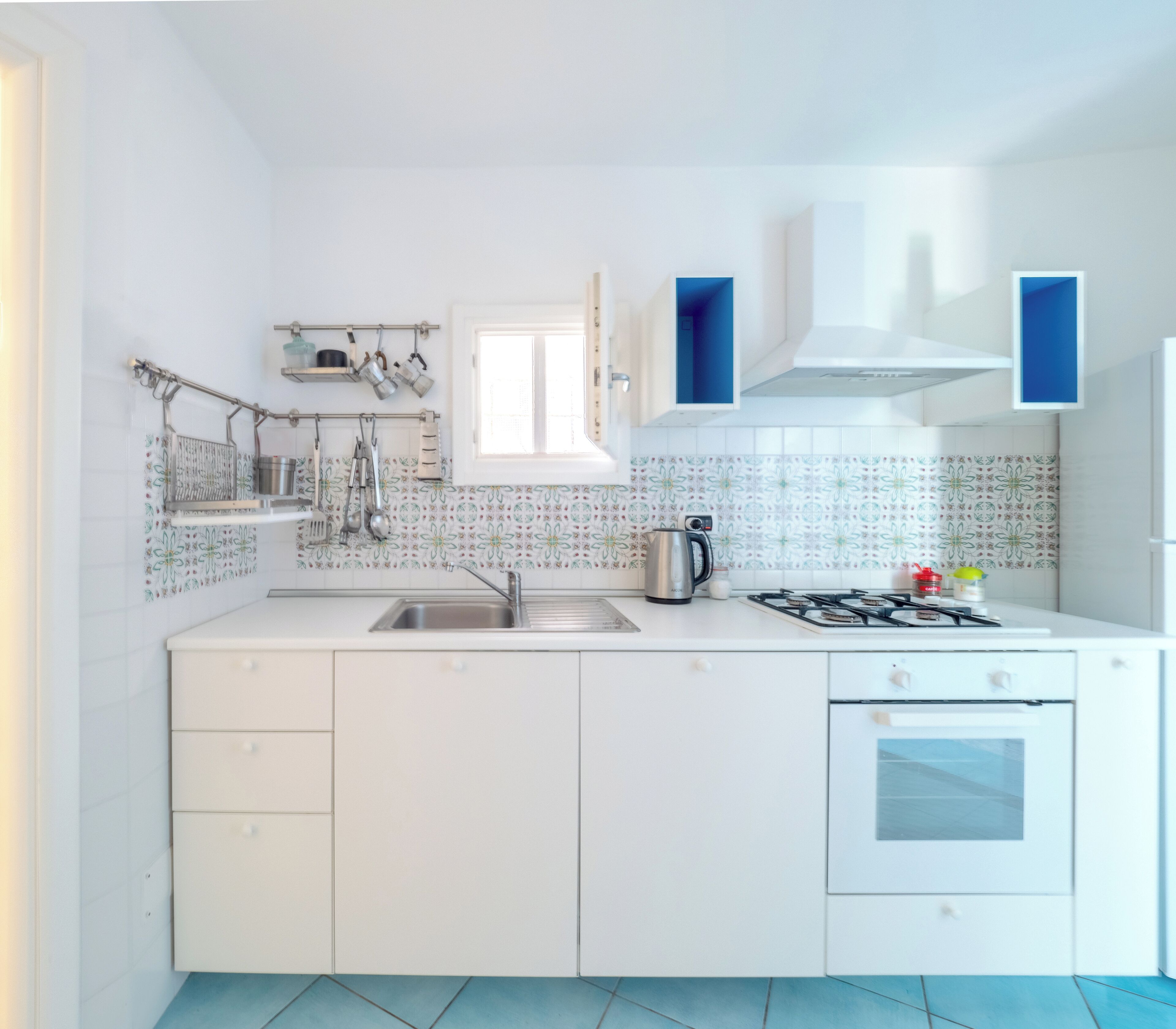 A modern kitchen with white cabinets, a gas stove, a sink, and a window above the countertop.