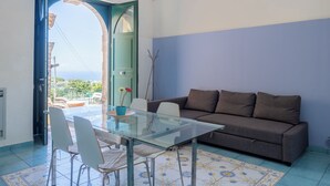 A room with a glass table, white chairs, a brown sofa, and a view through an open door. - Antica Residenza la Vela (Meta)