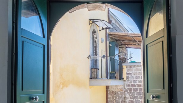 An open door leading to a balcony with a table, chairs, and a view of a building with a stone facade. - Antica Residenza la Vela (Meta)