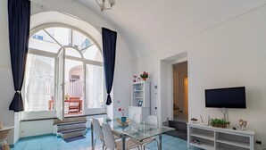 A modern living room with a glass dining table, white shelves, a flat-screen TV, and a large window with curtains. - Antica Residenza la Vela (Meta)