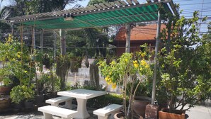 Un espace extérieur aménagé, abrité et doté de tables et de bancs, entouré de plantes en pot et surmonté d’une pergola.