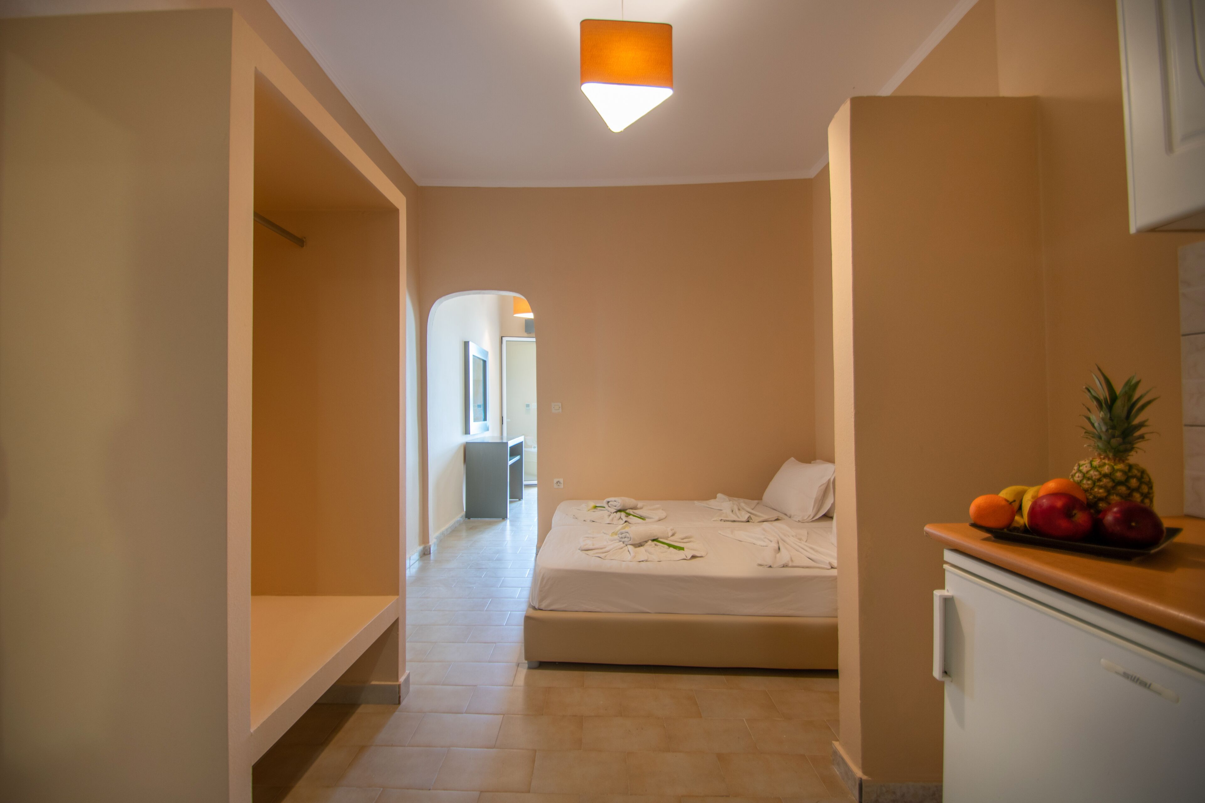 A hotel room with a bed, a small kitchenette, and a fruit bowl on the counter.