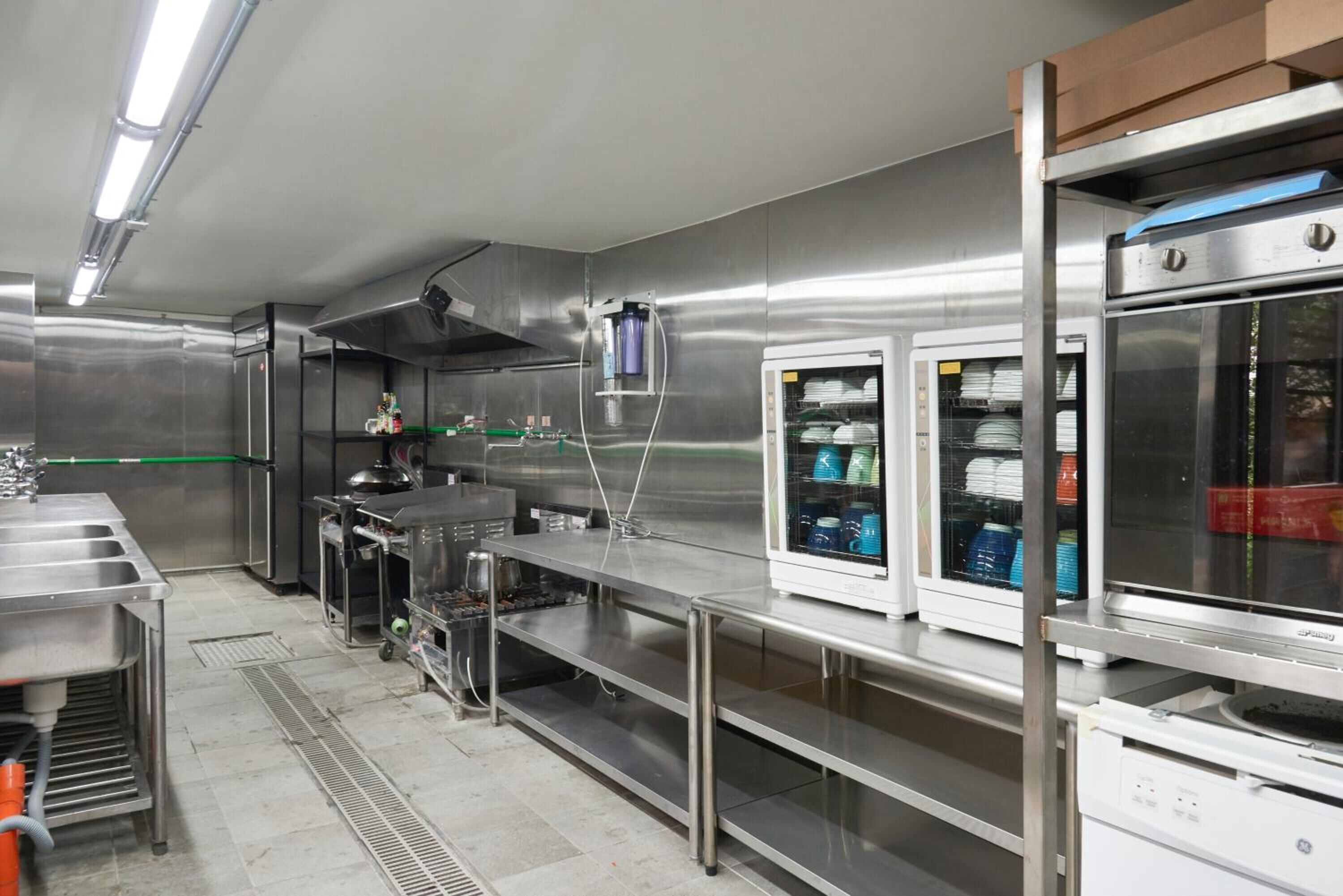 A commercial kitchen with stainless steel surfaces, a ventilation hood, and a walk-in refrigerator.