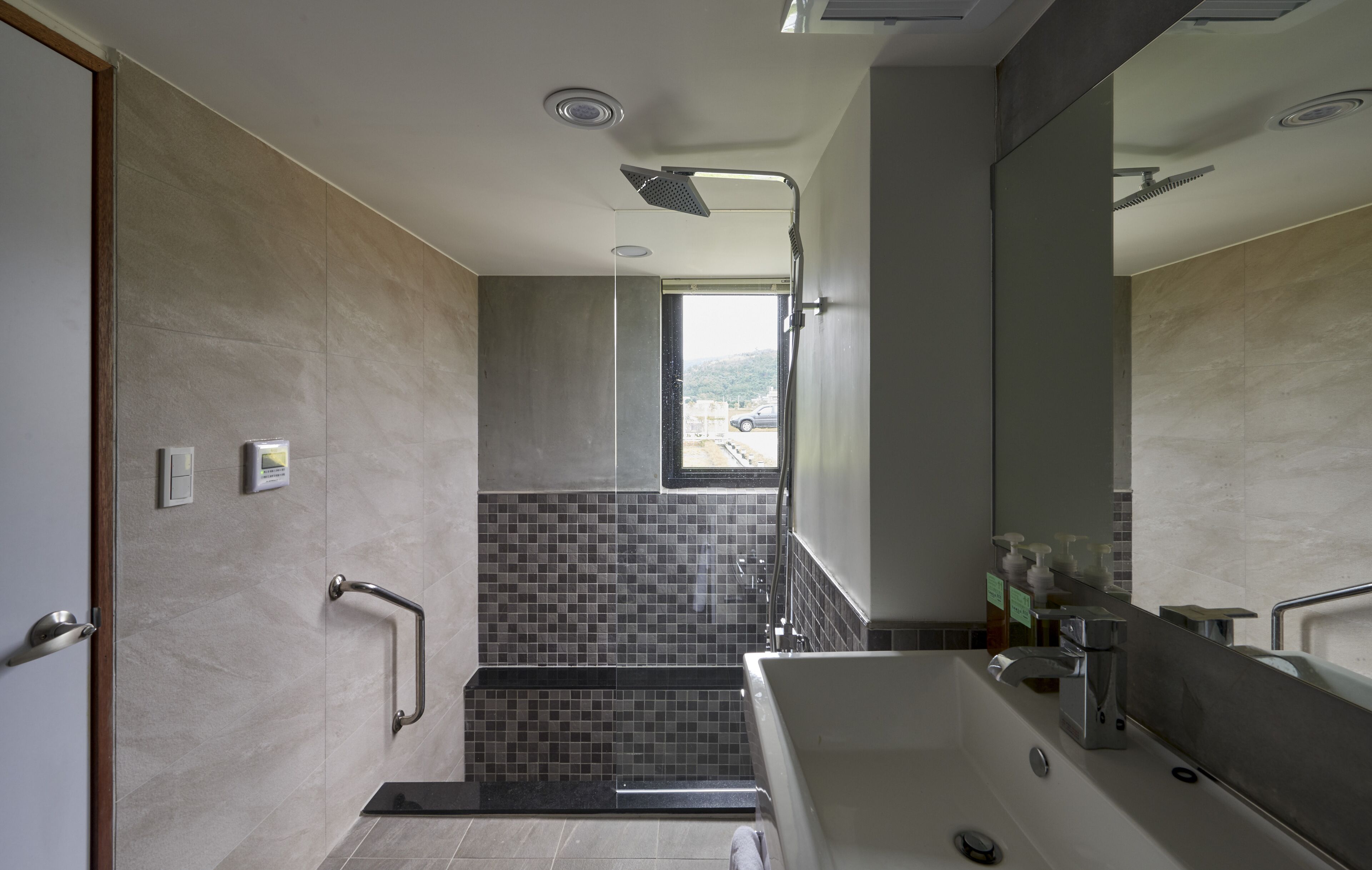 Een moderne badkamer met een douche, een bad, een handgreep en een raam.