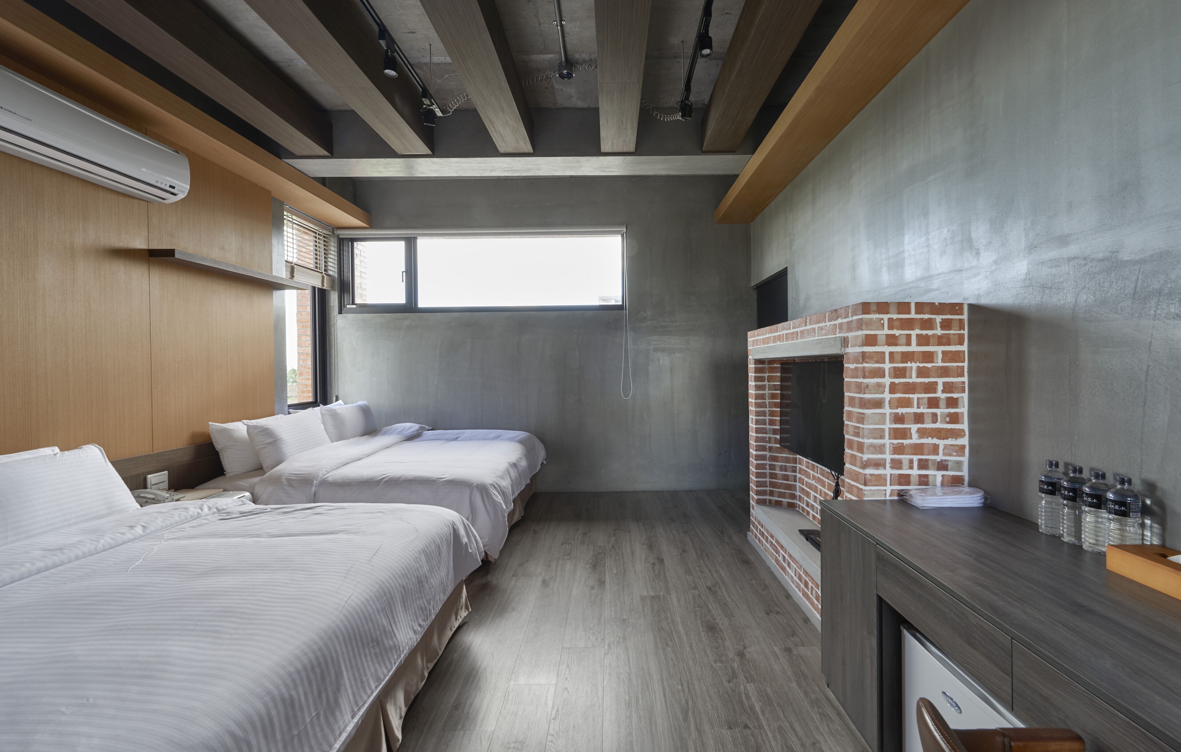 A modern hotel room with two beds, a brick fireplace, and a wooden ceiling.