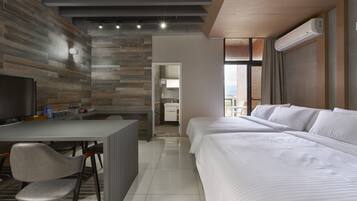 A modern hotel room with a wooden wall, a desk with a chair, a large bed, and a bathroom visible through an open door.