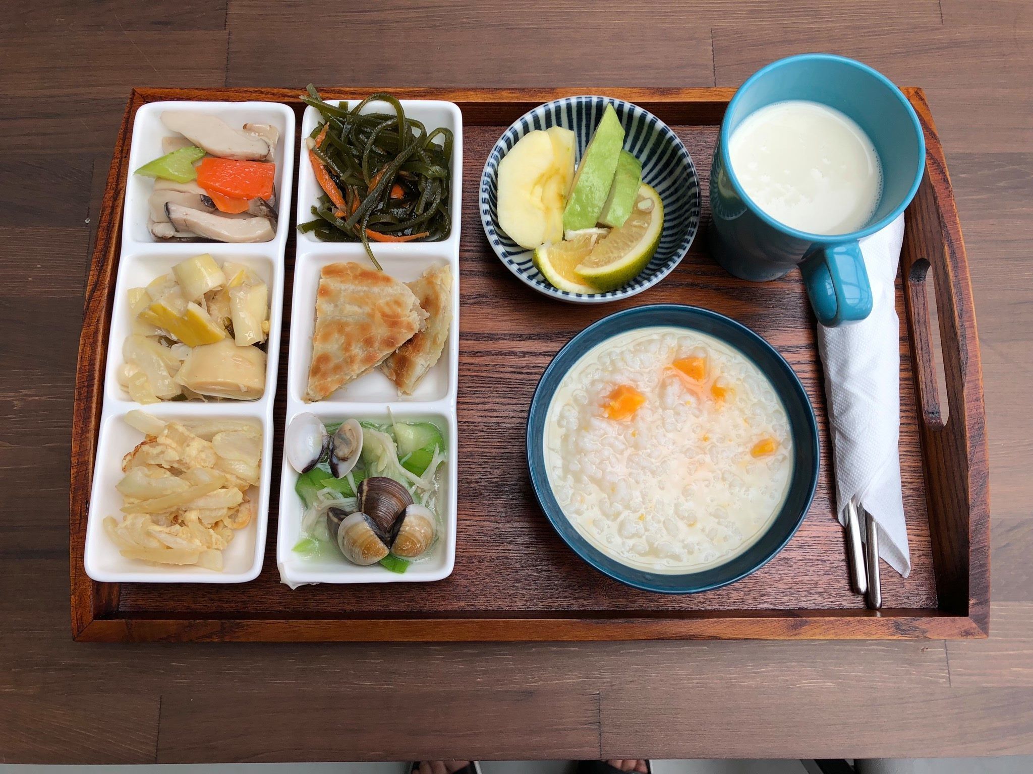 A wooden tray with various food items including a bowl of rice, a bowl of soup, and several small dishes containing different foods.