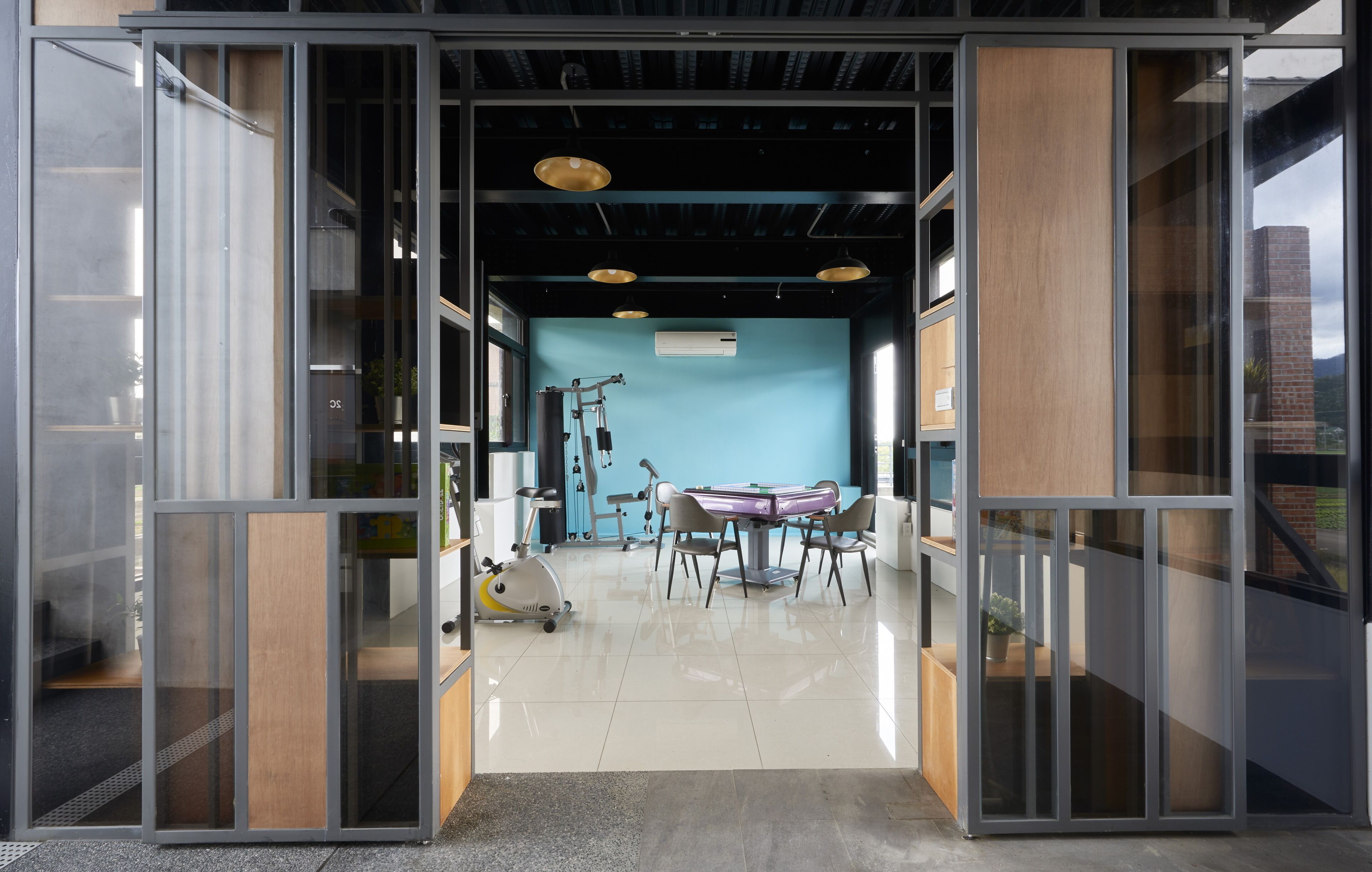 Un espacio de oficina diáfano con una pared azul, una mesa de ping-pong, equipo de ejercicio y un amplio ventanal.