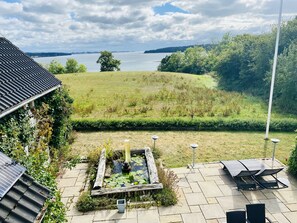 A patio with a pond, solar panels, and a view of a lake. - Naturperlen (Rodekro)