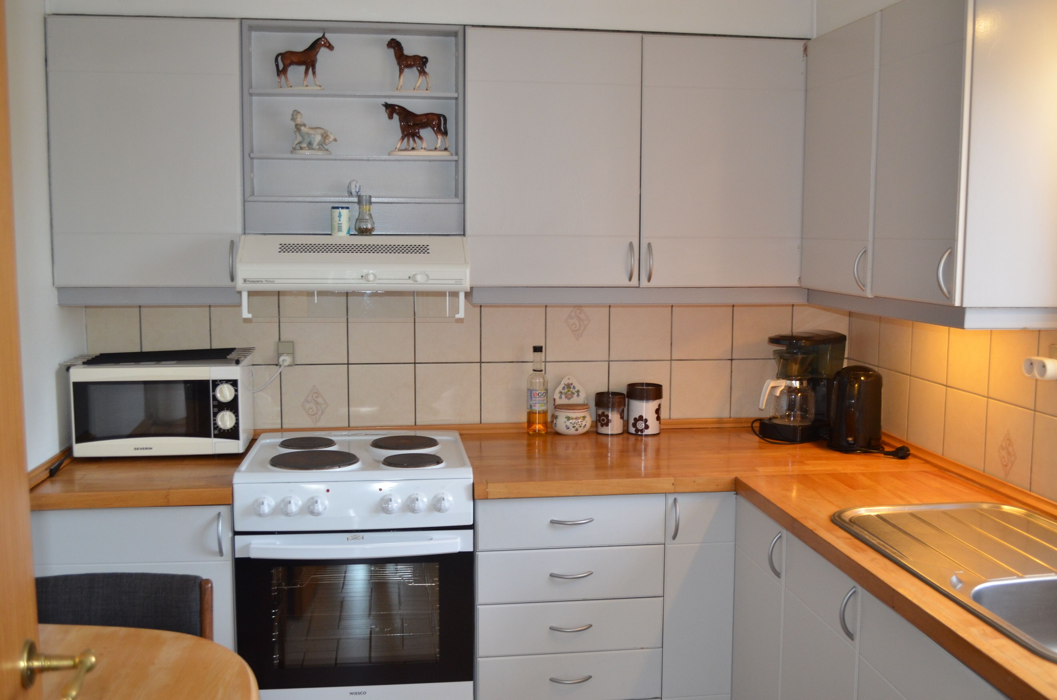 A kitchen with white cabinets, a microwave, a stove, and a coffee maker.