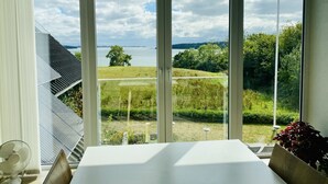 A room with a large window offering a view of a lake, grassy fields, and trees. - Naturperlen (Rodekro)