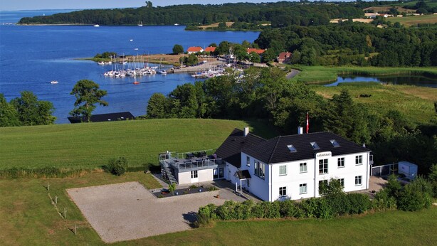 A white building with a sloped roof, a gravel driveway, and a small patio area. - Naturperlen (Rodekro)