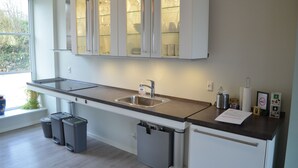 A modern kitchen with a stainless steel sink, a built-in oven, and a window with a view of greenery. - Naturperlen (Rodekro)