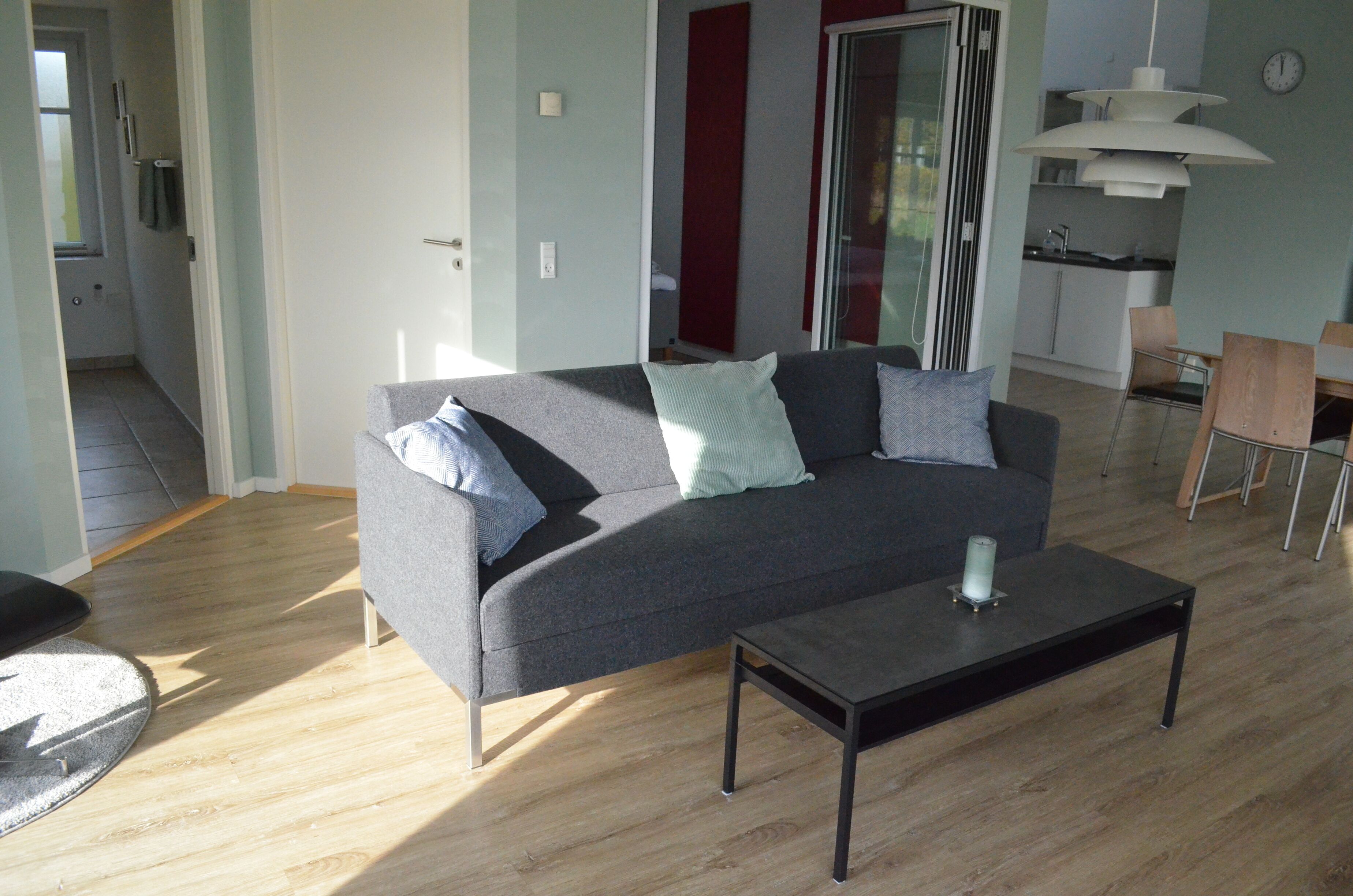 A modern living room with a grey sofa, a small table, and a kitchen area in the background.