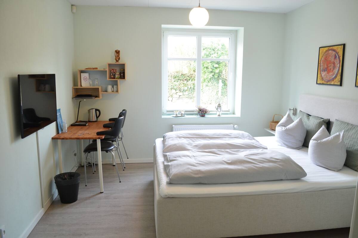 A bedroom with a bed, a desk, and a window.