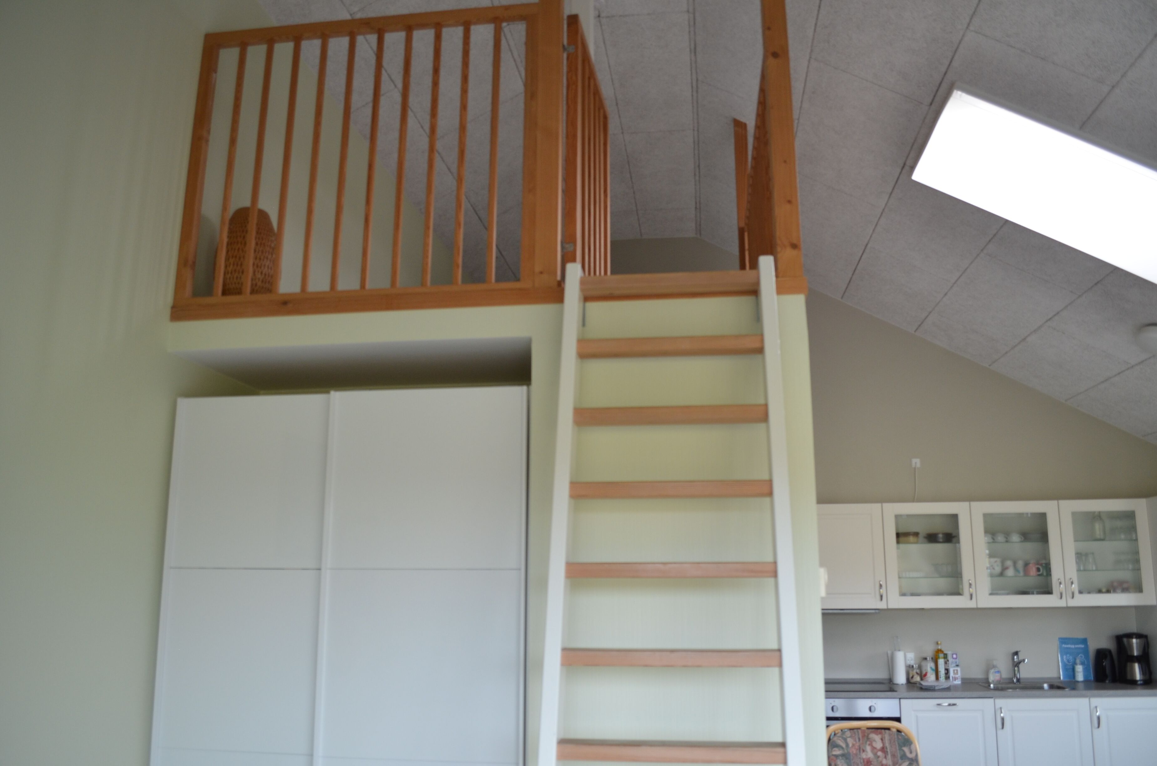 Une cuisine avec des meubles blancs, un escalier en bois et une lucarne.