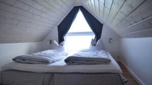 A small, triangular attic bedroom with a sloped ceiling, two beds with white bedding, and a large window at the peak. - Naturperlen (Rodekro)