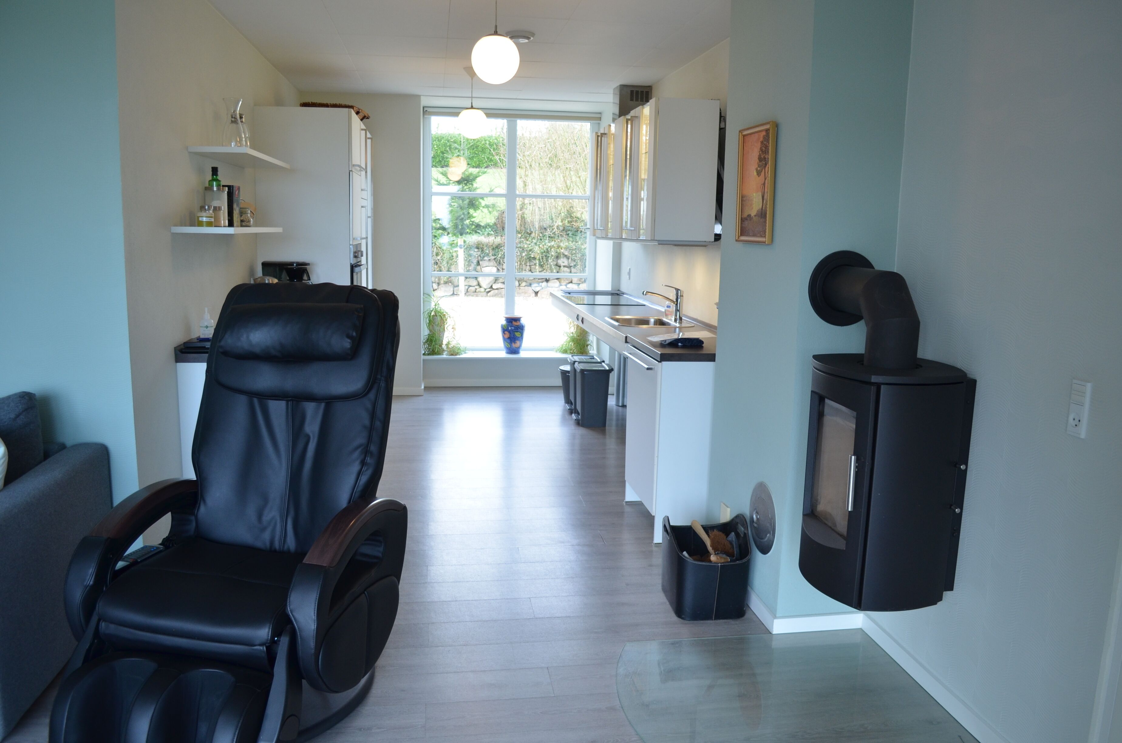 Une cuisine moderne avec un fauteuil en cuir noir, des armoires blanches et une grande fenêtre donnant sur un paysage verdoyant.
