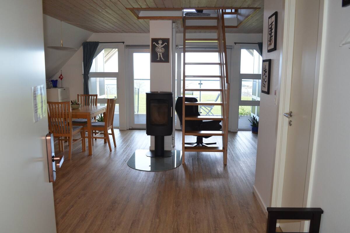 A spacious room with a dining area, a fireplace, a loft bed, and a view of the outdoors.