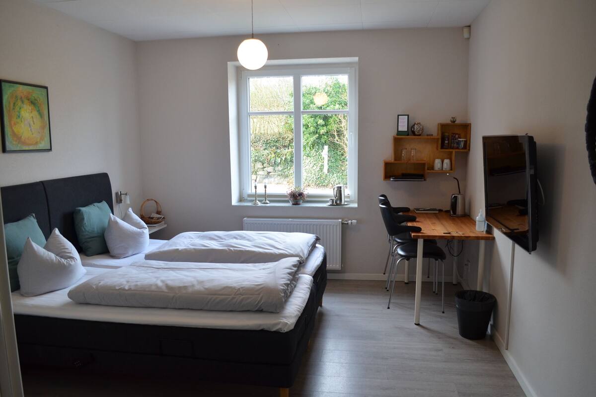 A bedroom with a bed, a desk, and a window.