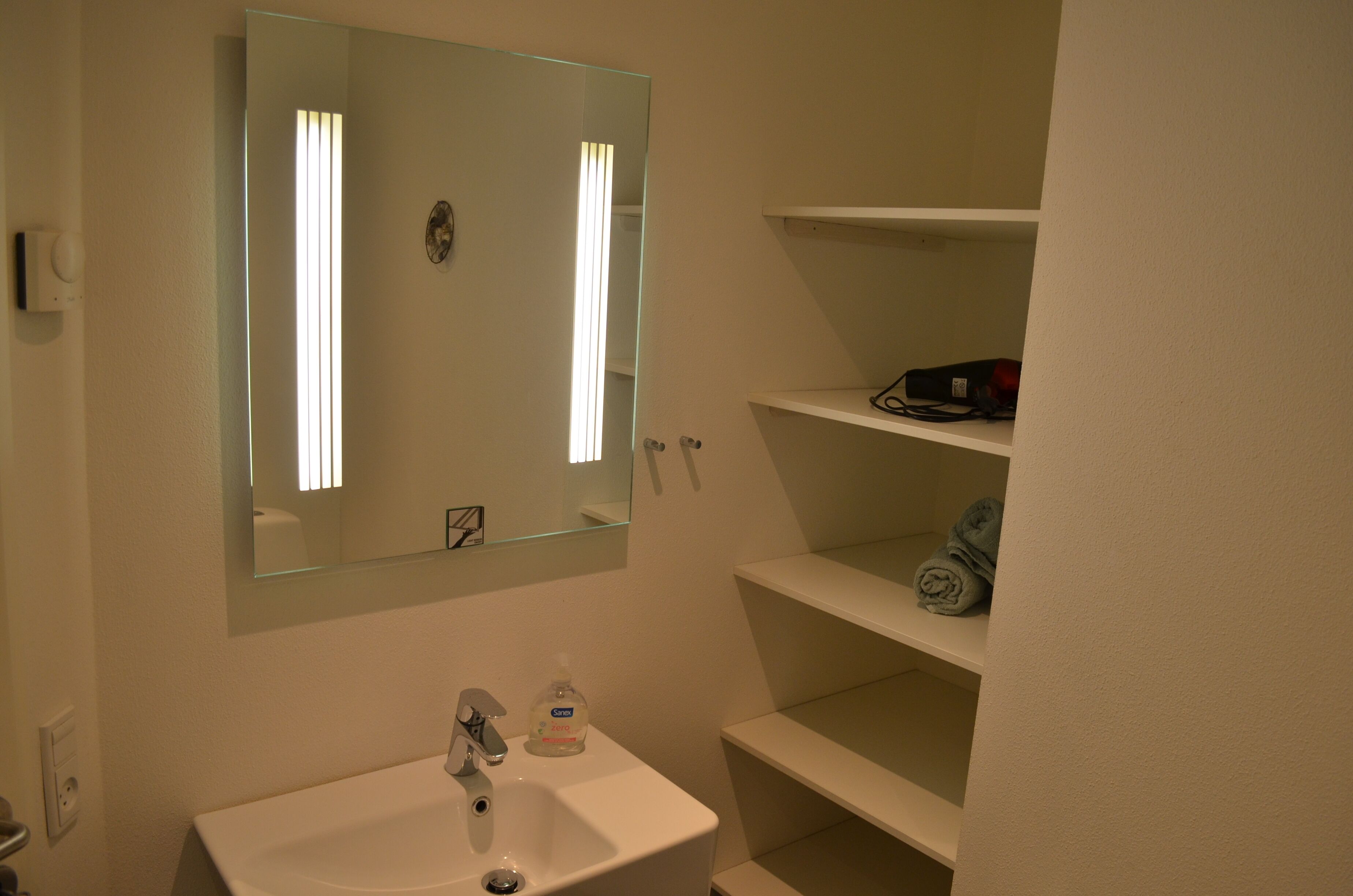 A bathroom with a white sink, a mirror, and a shelf with folded towels.